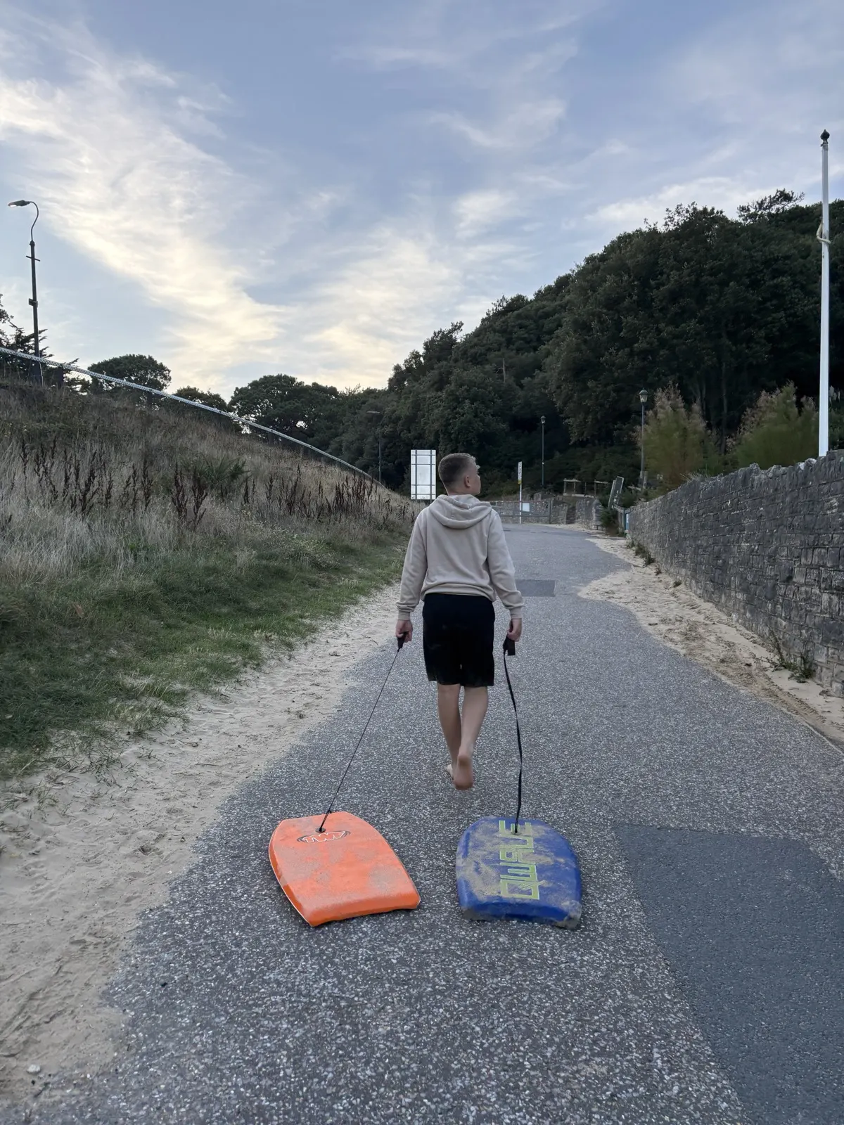 Ronnie walking up a sandy path from the beach, towing two bodyboards behind him on their leashes